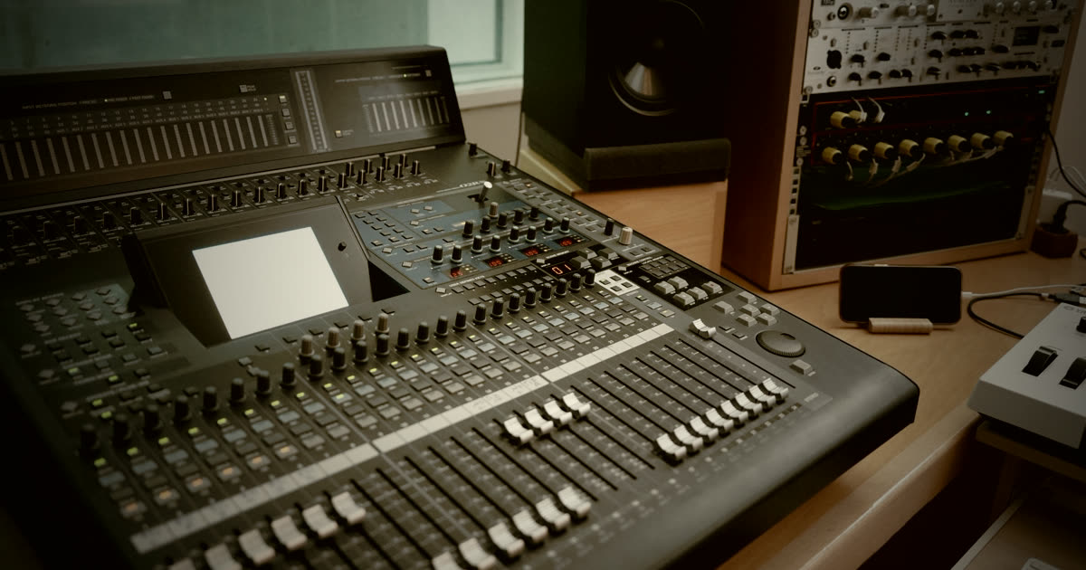 A close-up view of an audio mixing console featuring a variety of faders, knobs, and butto